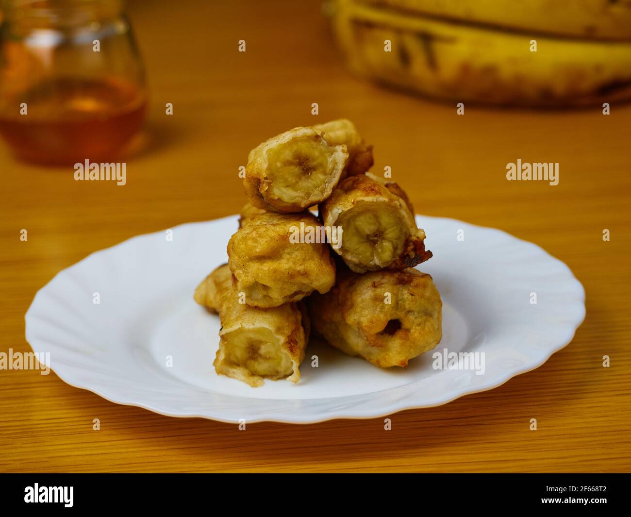 Gebratene Scheiben der reifen Kochbanane auf einem weißen Gericht Dekoriert mit Bananen und Honig Stockfoto