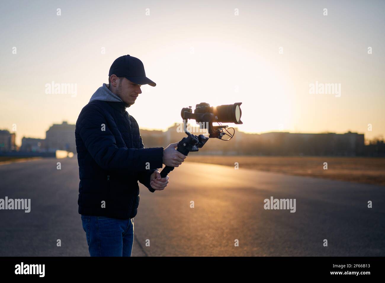 Junger Mann beim Filmen mit Kamera und Gimbal. Filmemacher, der bei Sonnenaufgang gegen die Stadt steht. Prag, Tschechische Republik Stockfoto