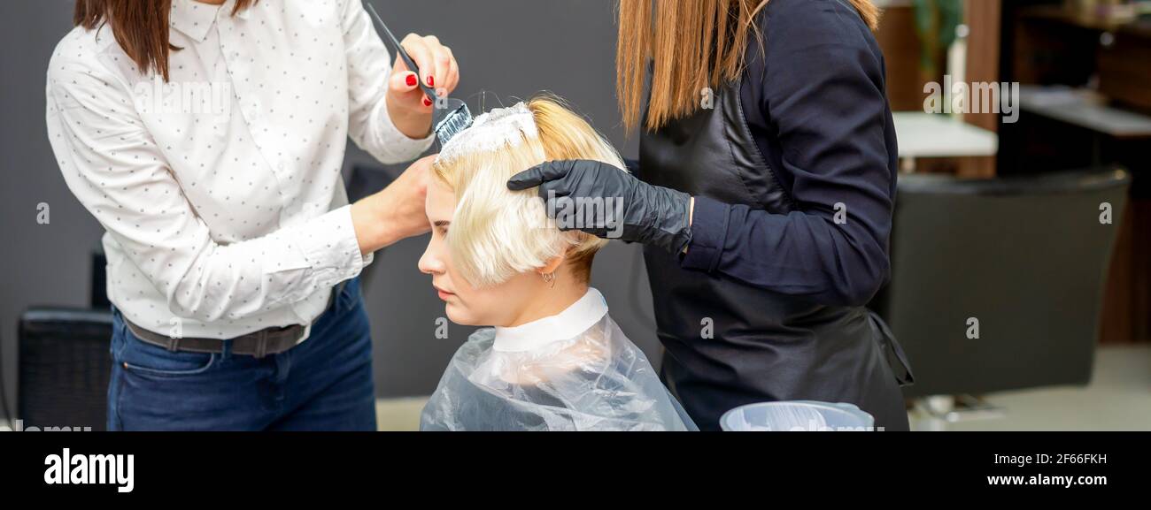 Zwei weibliche Friseure färben Haare von jungen kaukasischen Frau in Friseursalon Stockfoto