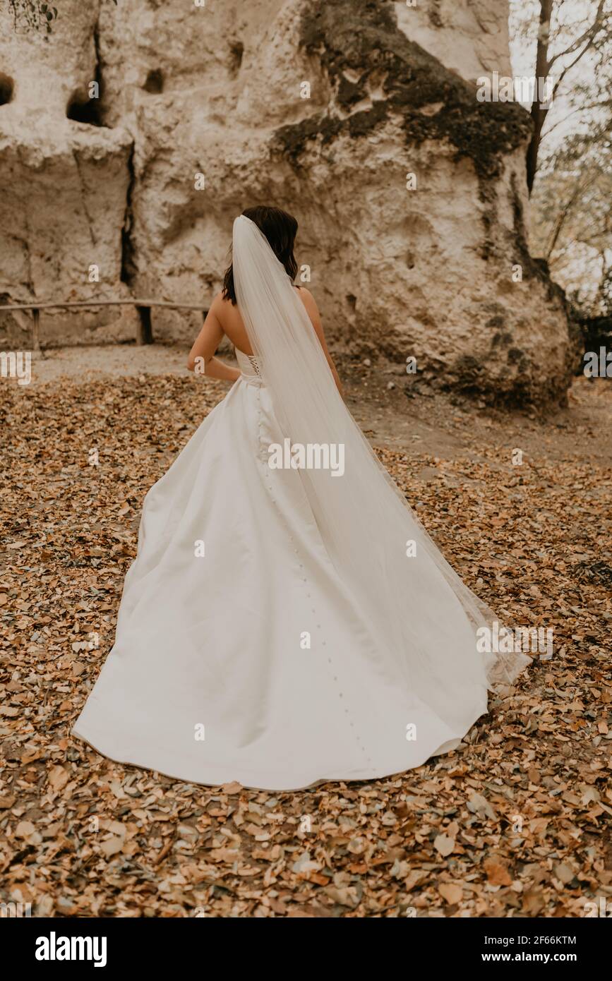 Junge Frau Braut in weißen Brautkleid mit langen Schleier laufen weg durch Herbstwald auf gefallenen orangefarbenen Blättern in den Berg. Brunette mit kurzen Haaren Stockfoto