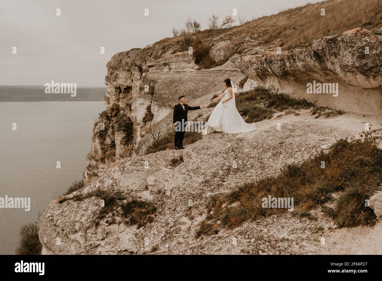 Liebevolle Paar Hochzeit frisch vermählt im Freien. Braut in weißem Kleid langen Schleier und Bräutigam in Anzug Spaziergang im Sommer fallen auf Berg über dem Fluss. sonnenaufgang. Mann Stockfoto