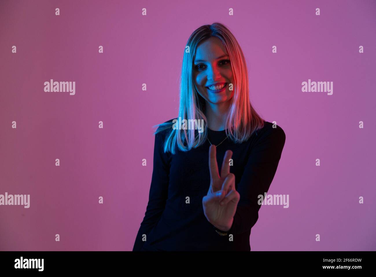 Junge blonde Frau von Neonlicht beleuchtet macht den Sieg unterschreiben Sie mit ihrer Hand Stockfoto
