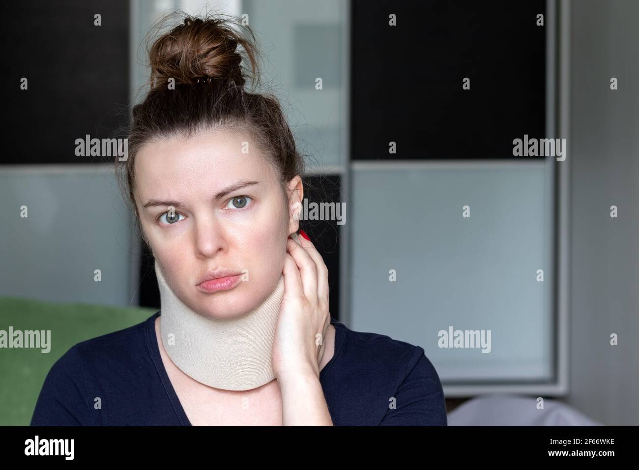 Frau mit zervikalen chirurgischen Kragen Gefühl Schmerzen im Hals in Zuhause vor einem verschwommenen Hintergrund Stockfoto