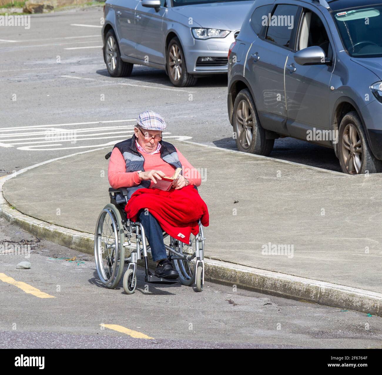 Ein alter Herr mit einem Bein saß im Rollstuhl und las einen Buchen Stockfoto