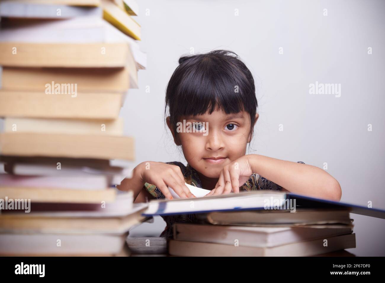 Nettes kleines Mädchen mit Haufen von Büchern zu studieren und Hausaufgaben zu Hause machen Stockfoto