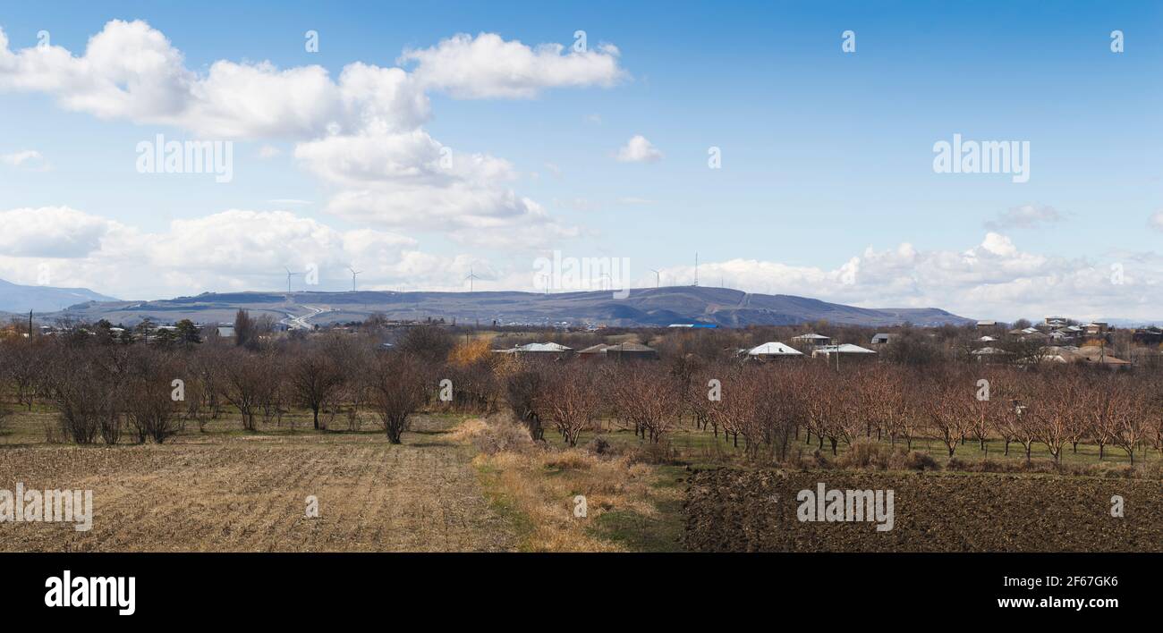 Ländliche Landschaft mit Windmühlen auf der Spitze des Hügels. Obstgärten und landwirtschaftliche Felder im Vordergrund. Stockfoto