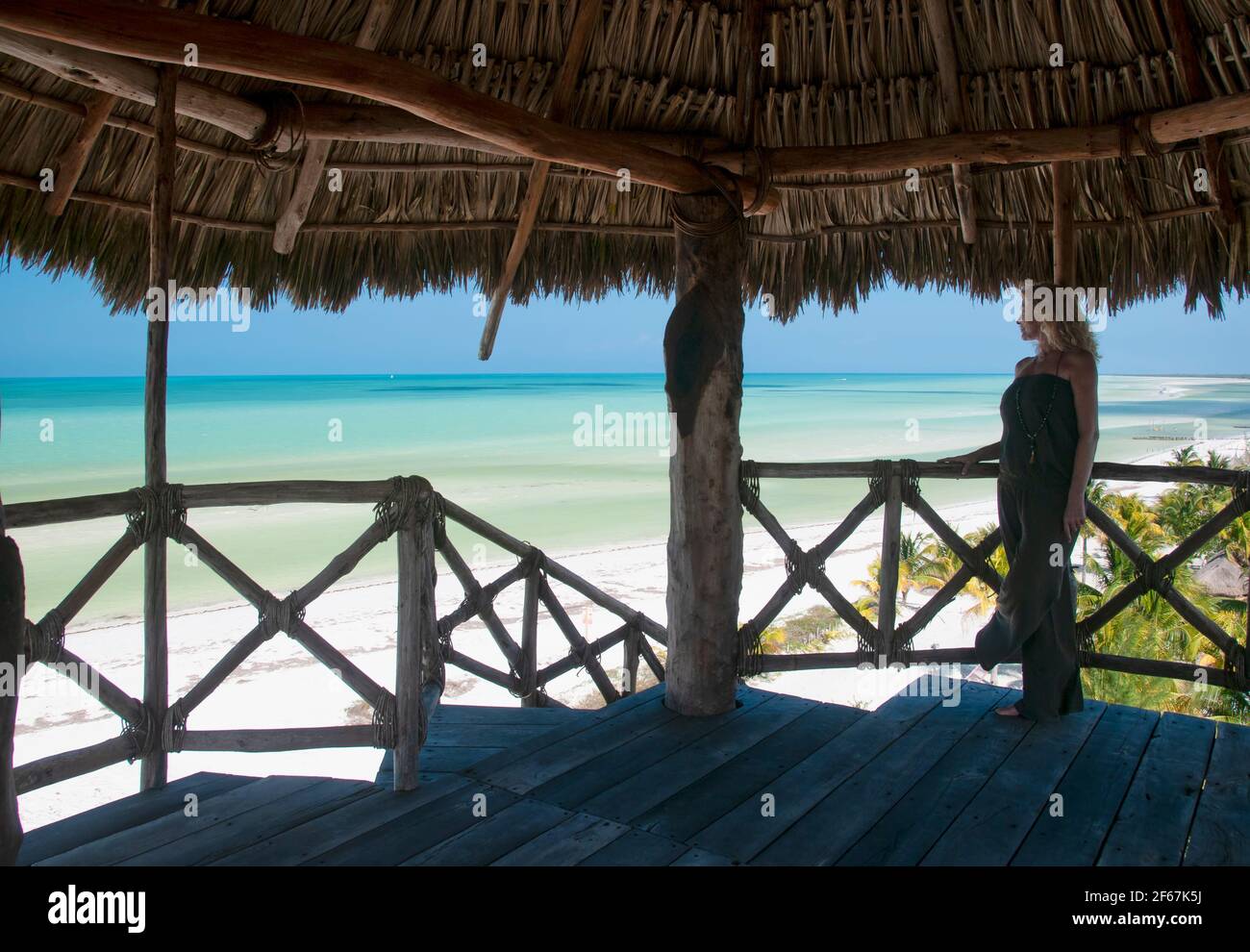 Eine junge blonde Frau, die auf einem hölzernen Aussichtsturm steht, blickt über den Horizont über das Karibische Meer auf der Insel Holbox in Mexiko. Konzept Reise Tour Stockfoto