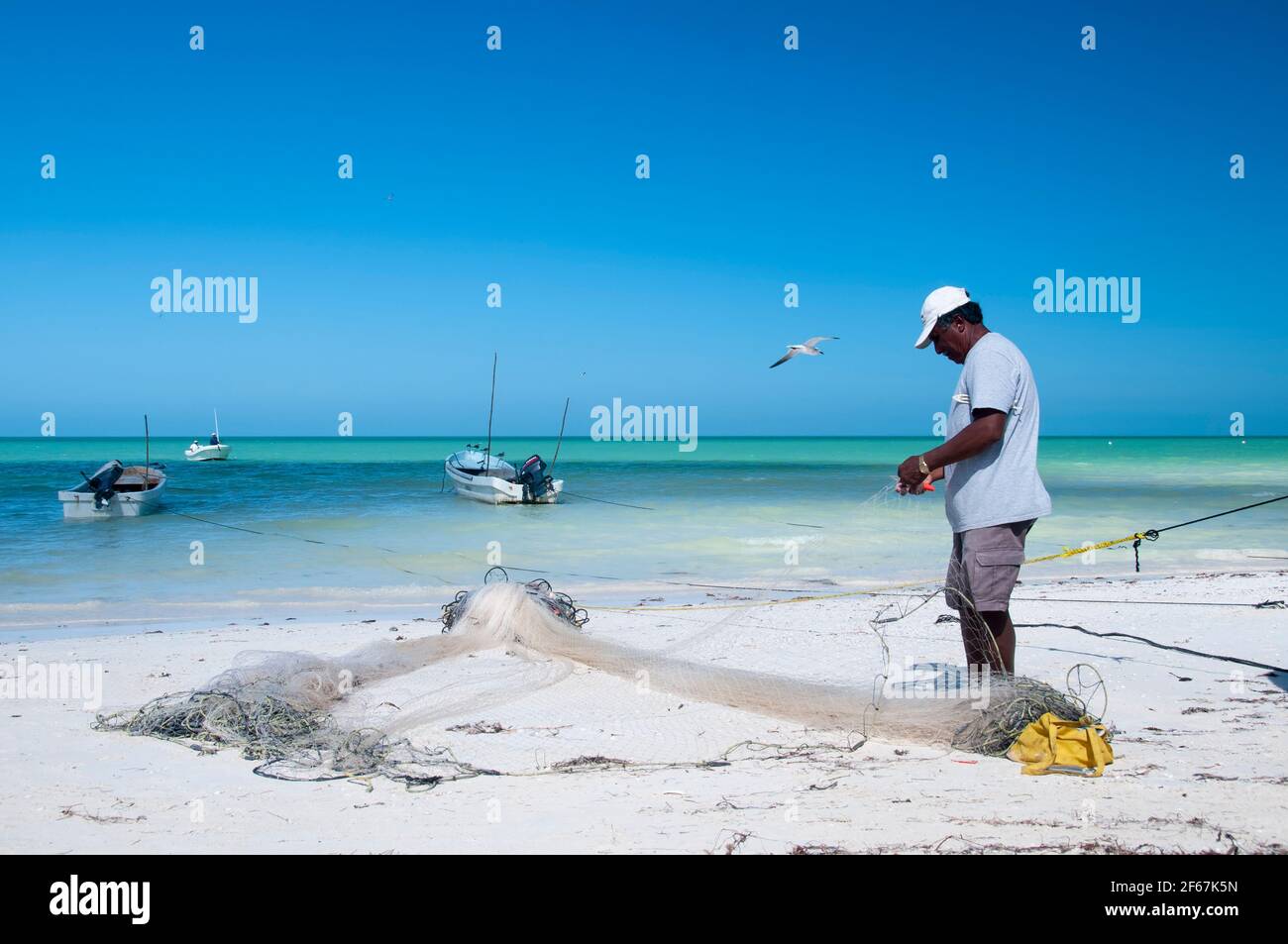 Ein Fischer am Strand von Holbox Island in Mexiko repariert seine Netze am Strand am frühen Morgen. Im Hintergrund das Karibische Meer und klein Stockfoto