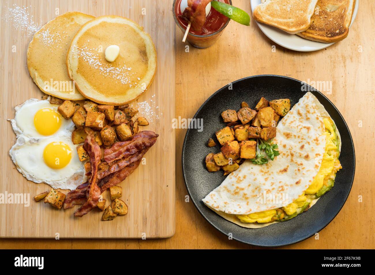Huevos Rancheros und ein Slam-Frühstück. Drei Rühreier in einer Mehl-Tortilla mit gebratenen Bohnen, Guacamole und geriebenem Käse. Zwei Eier sonnig si Stockfoto