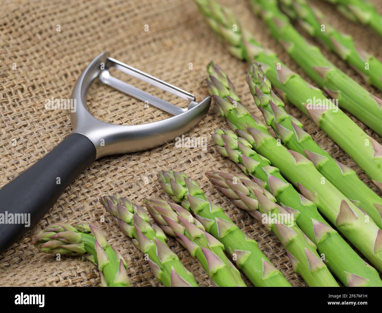 Grüner Spargel mit Schäler auf Jutesack Stockfoto