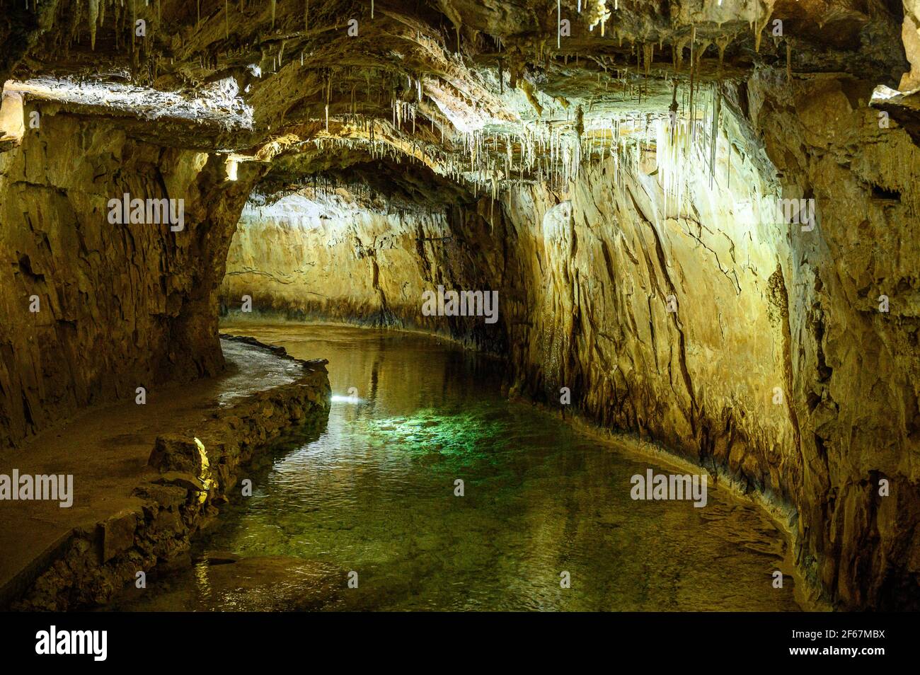 Gehweg, der entlang des unterirdischen Flusses führt, der durch den Tunnel fließt. Kleine Stalaktiten, die vom Höhlendach hängen. Vercors Mountains, Frankreich. Stockfoto