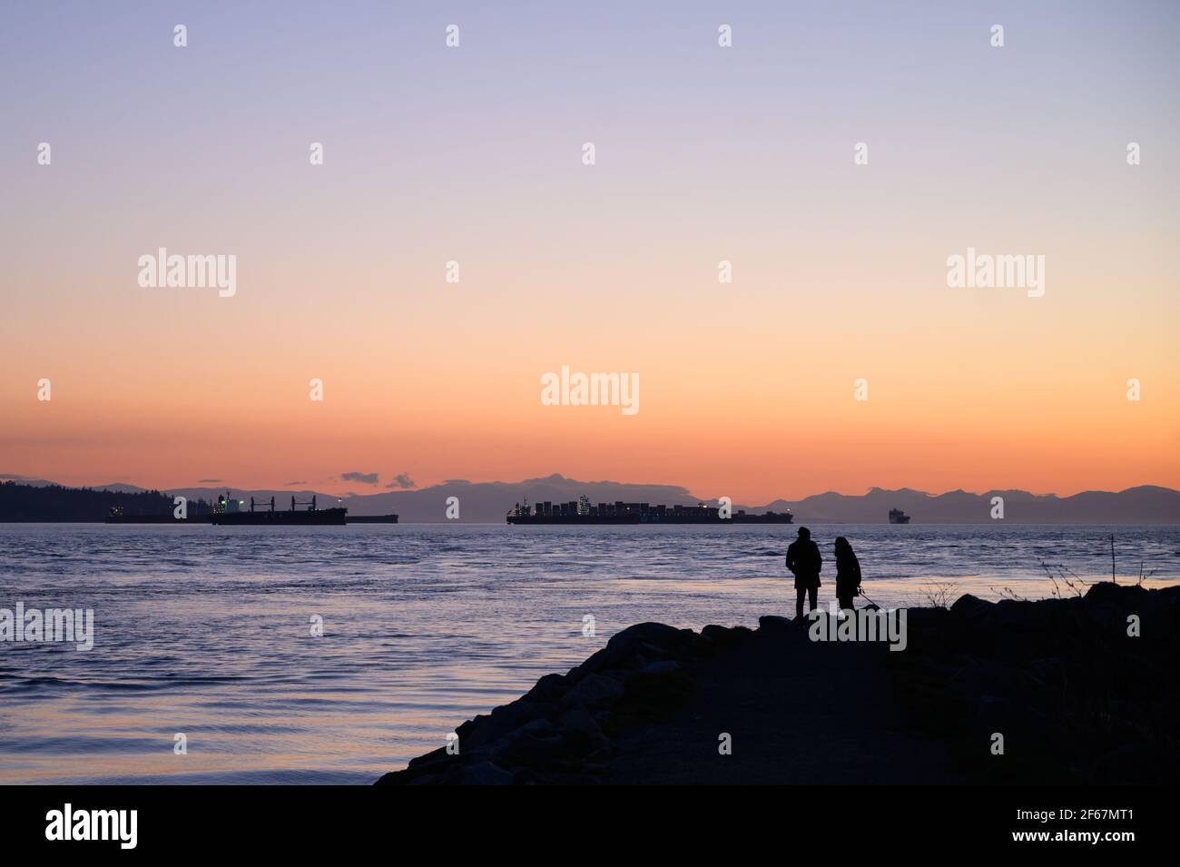 Ein Paar beobachtet den Sonnenuntergang vom Ambleside Park in West Vancouver. West Vancouver, British Columbia, Kanada. Stockfoto