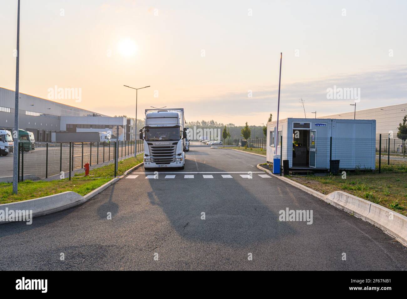Vorderansicht des weißen schweren Lkws, der am Torhaus des Verteilungslagers angehalten wurde. Foto gegen die Morgensonne. Transport und Logistik. Stockfoto