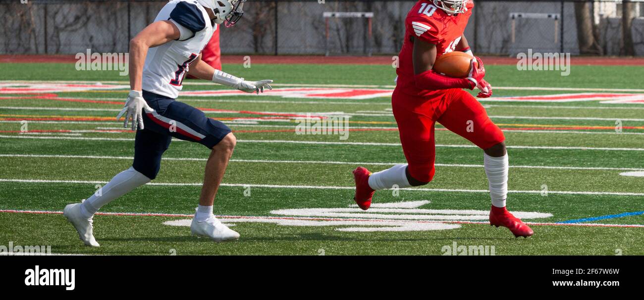 Breiter Empfänger läuft weg vom Verteidiger, der versucht, ihn während eines Highschool-Fußballspiels zu bekämpfen. Stockfoto