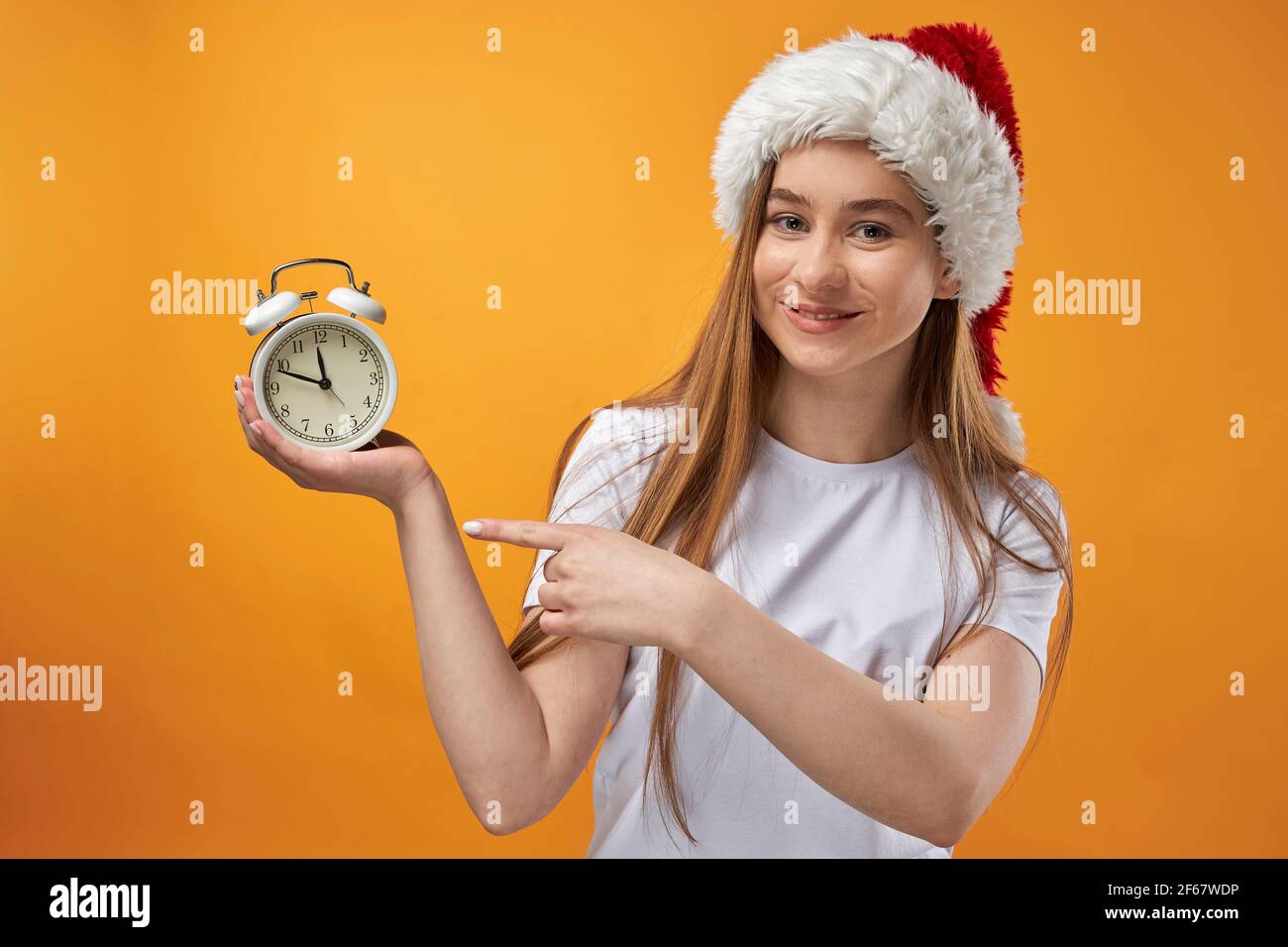 Frau in Weihnachtsmann Hut mit Wecker auf Hintergrund isoliert. Stockfoto