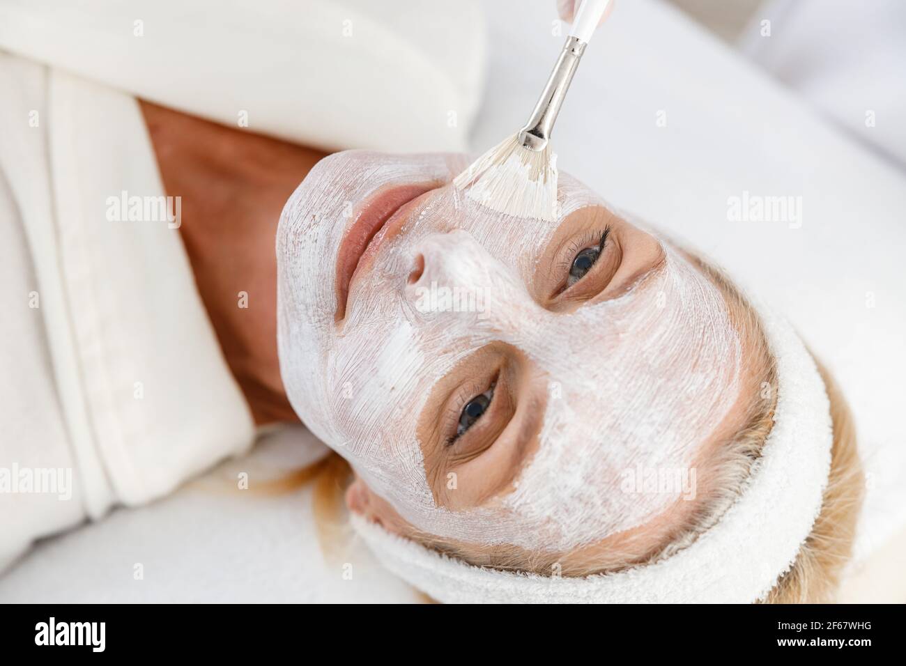 Nahaufnahme Foto der Kosmetikerin Anwendung Ton Gesichtsmaske auf Gesicht einer älteren Frau Stockfoto