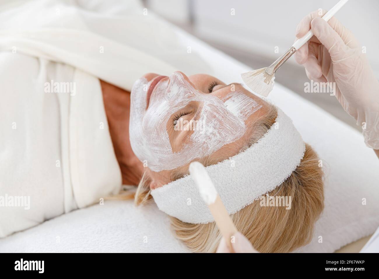 Nahaufnahme Foto der Kosmetikerin Anwendung Ernährung Gesichtsmaske auf ältere Frau Gesicht. Stockfoto