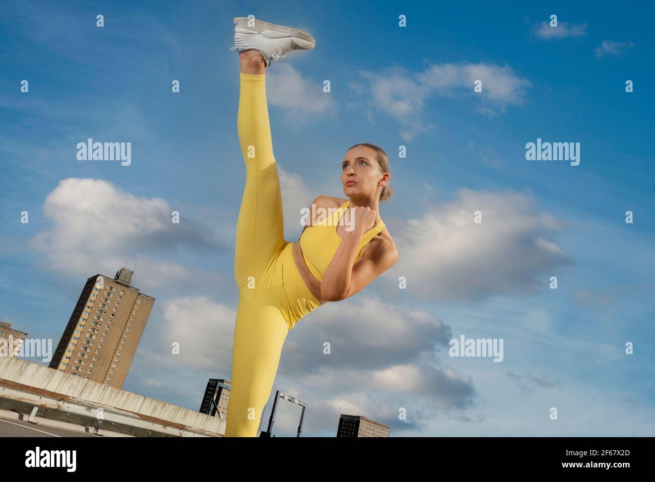 Attraktive sportliche Frau trägt gelbe activewear üben High-Kick-Übung draußen in einer städtischen Umgebung. Stockfoto
