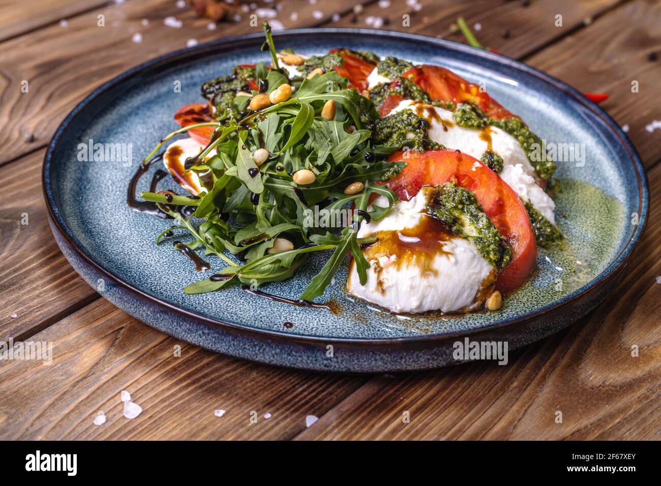 Tomatenscheiben und Mozzarella liegen auf einem mit Kräutern gewürzten Teller, garniert mit Chili und Zimt. Stockfoto