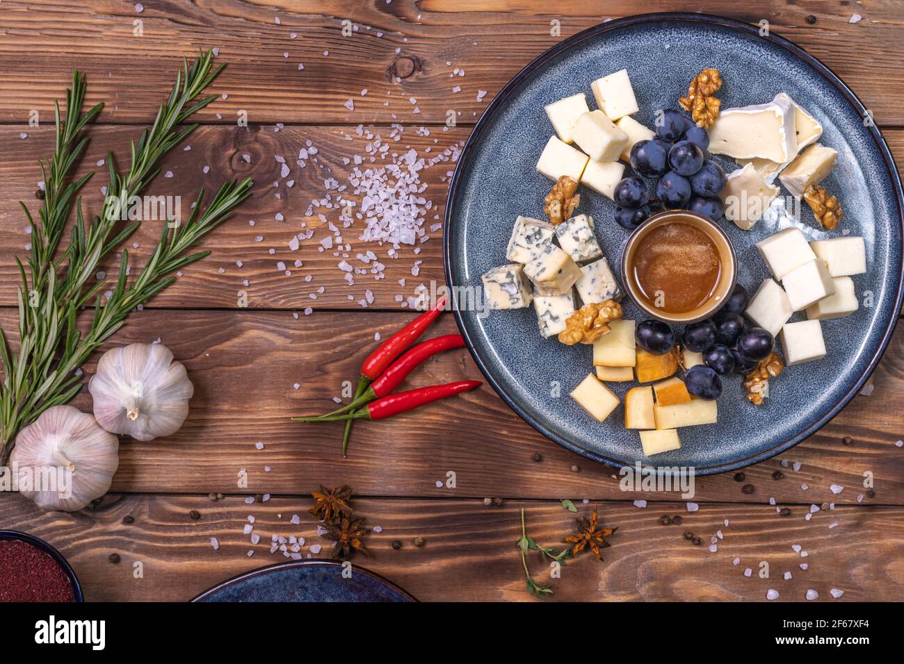 Ein Teller mit Käse, Honig, Trauben auf Holzgrund, mit Gewürzen, Rosmarin, Knoblauch verziert. Restaurant-Service. Stockfoto