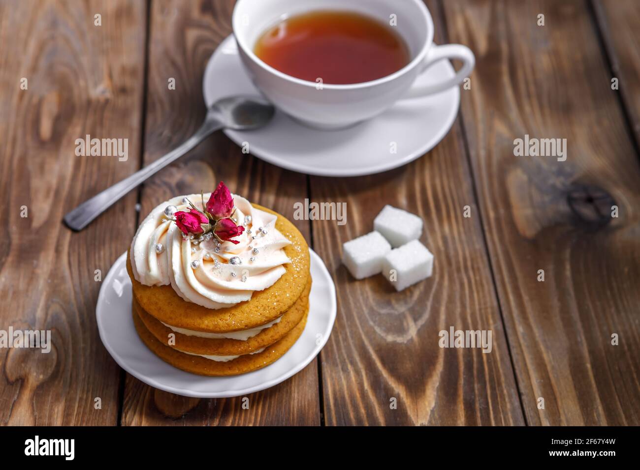 Biskuitkuchen mit Sahne, verziert mit kleinen Blumen und einer Tasse Tee. Das Konzept eines festlichen Leckerbissen. Handarbeit Stockfoto