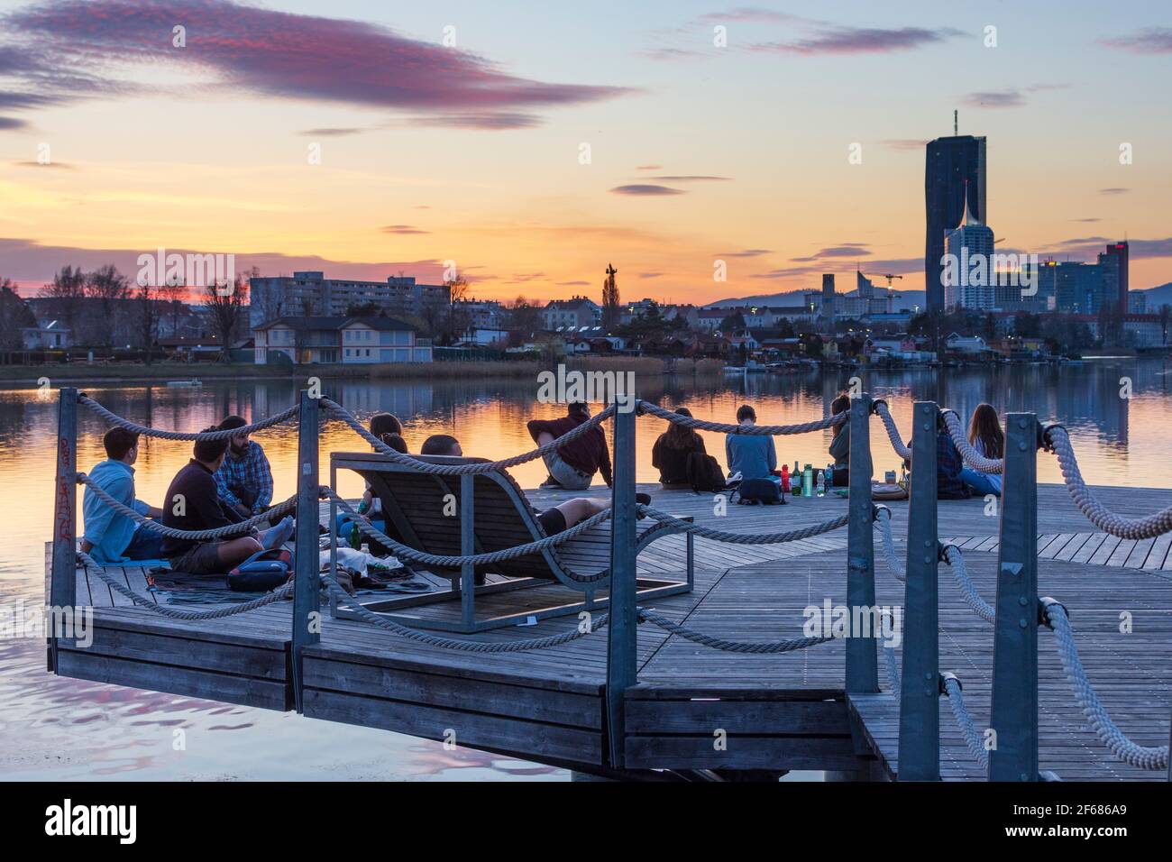 Wien, Wien: Junge Leute auf einer Plattform bei einer Party über dem Ochsenkelsee Alte Donau bei feurigem Sonnenuntergang, Gebäude der Donaucity, DC Tower 1, Coro Stockfoto