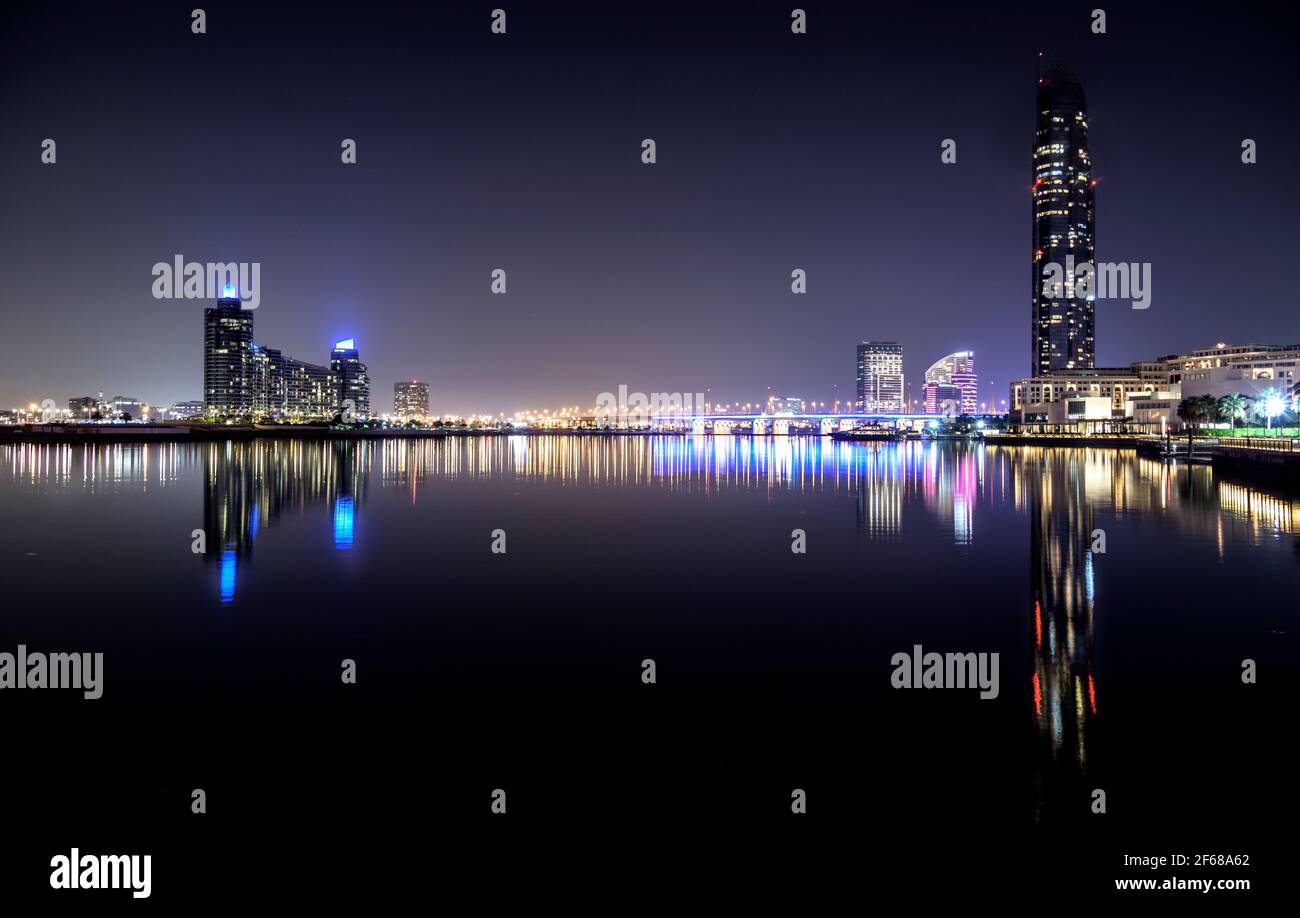 Wunderschöne Nachtansicht der beleuchteten Business Bay Brücke über das Wasser mit Reflexionen umgeben von majestätischen Wolkenkratzern, die in Dubai eingefangen wurden. Stockfoto