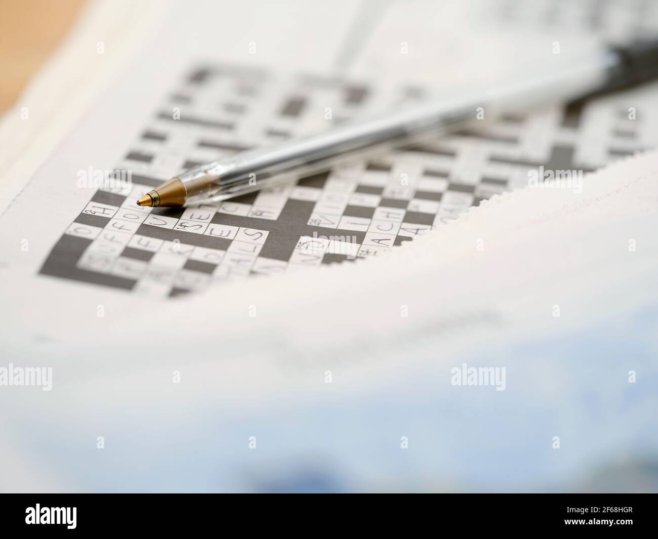 Ein Biro-Stift ruht auf einem teilweise ausgefüllten Kreuzworträtsel mit den Wörtern, die aus einem niedrigen Winkel betrachtet werden. Stockfoto