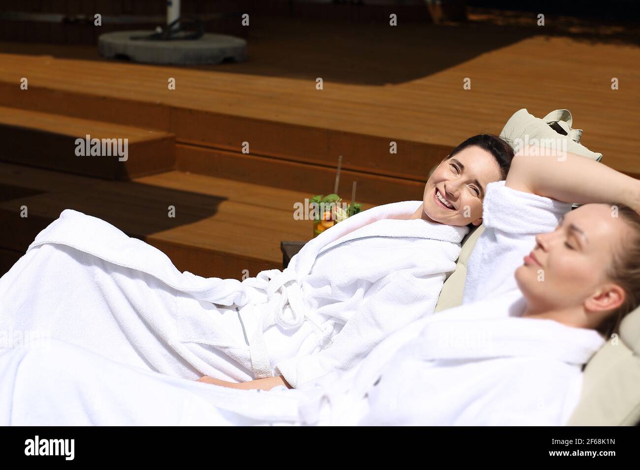 Pärchen sonnen sich auf den Sonnenliegen. Frauen entspannen sich in einem luxuriösen Spa. Zwei Frauen entspannen sich an einem sonnigen Sommertag auf Liegestühlen Stockfoto