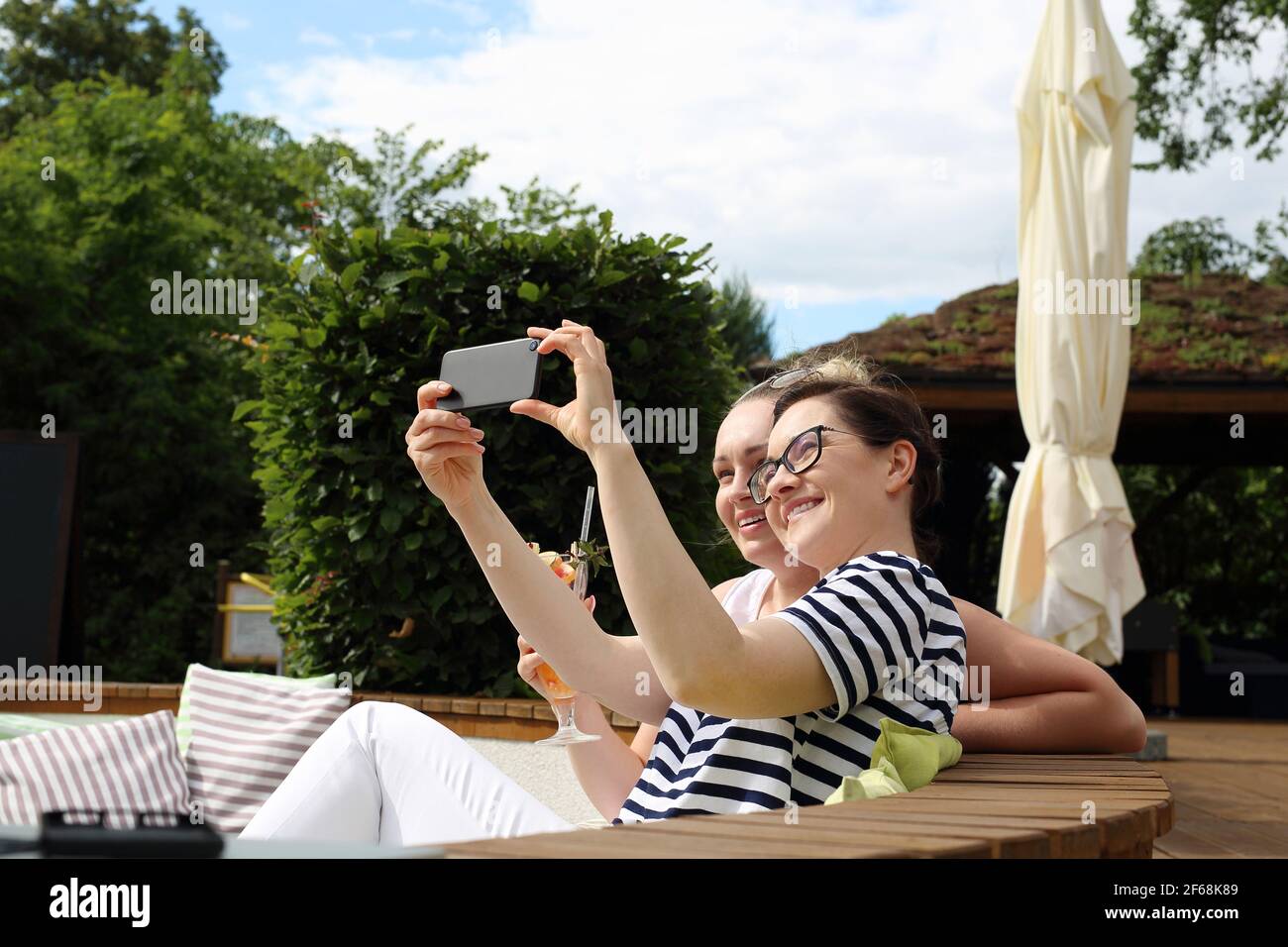 Fernarbeiten im Garten. Zwei Frauen arbeiten an einem Computer, während sie auf einem Gartenstuhl sitzen. Stockfoto