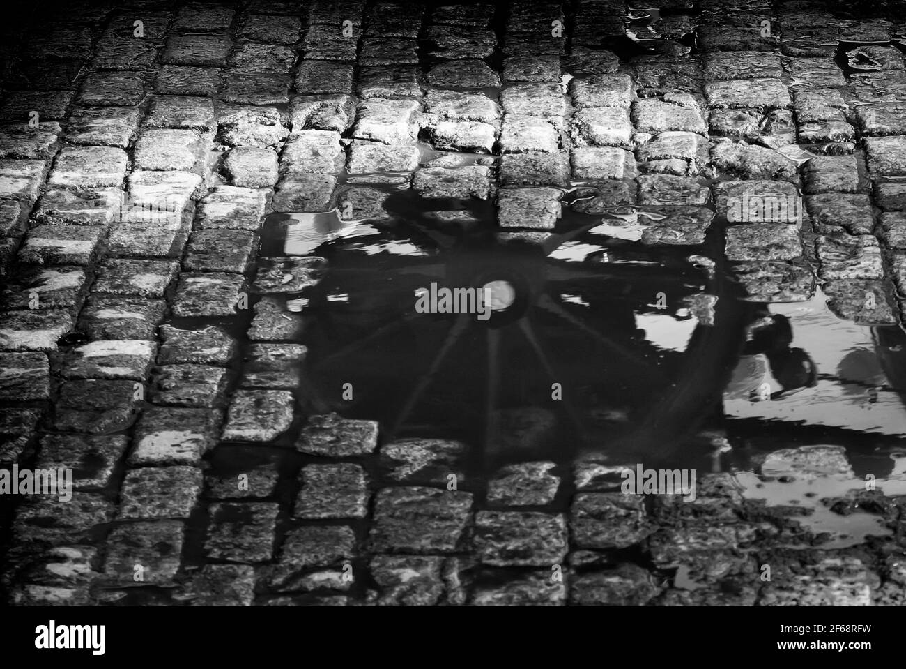 Das hölzerne Rad eines Pferdewagens spiegelt sich nach dem Regen in einer Wasserpfütze wider. Schwarzweiß-Foto. Stockfoto