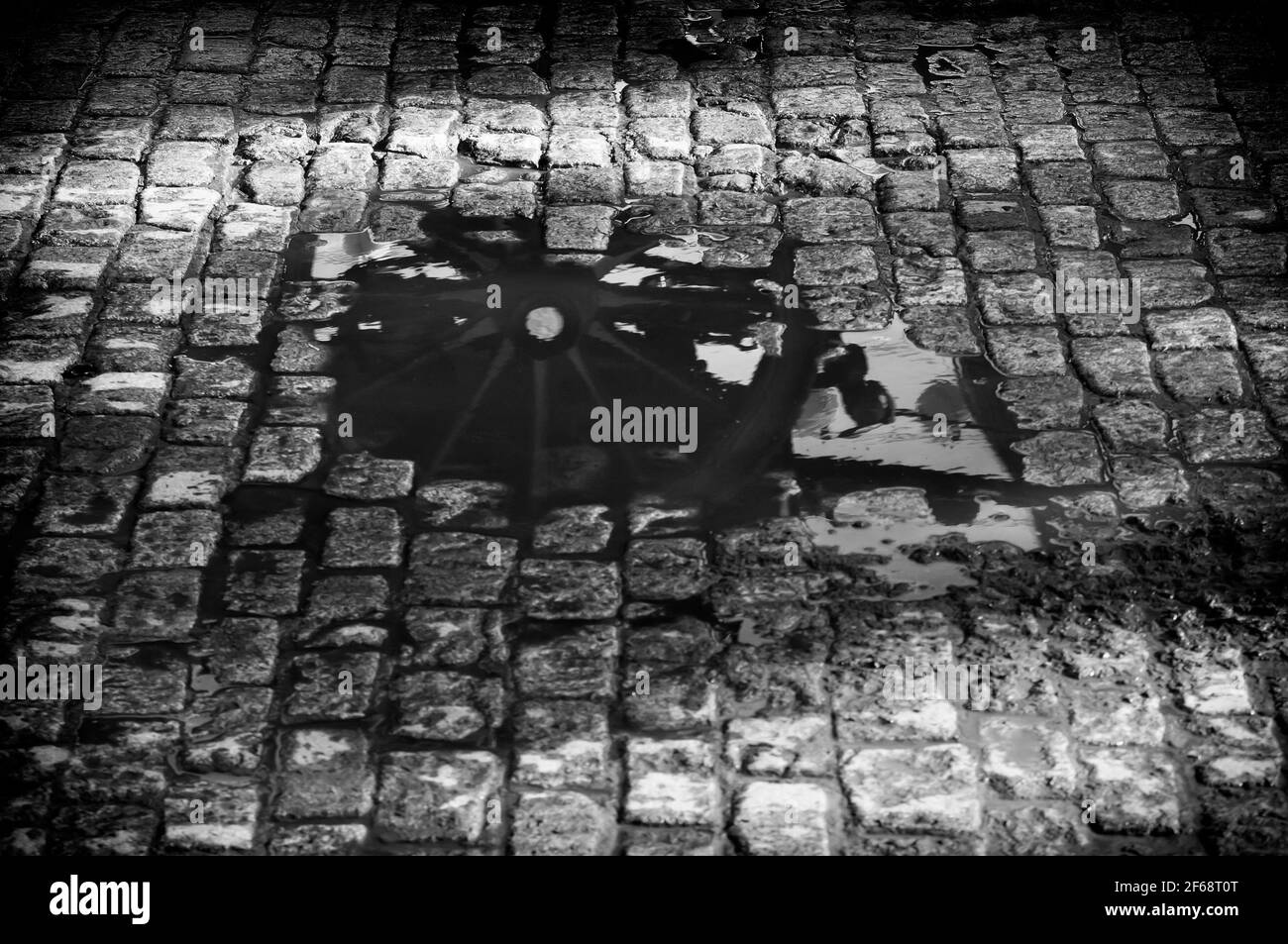 Das hölzerne Rad eines Pferdewagens spiegelt sich nach dem Regen in einer Wasserpfütze wider. Schwarzweiß-Foto. Stockfoto