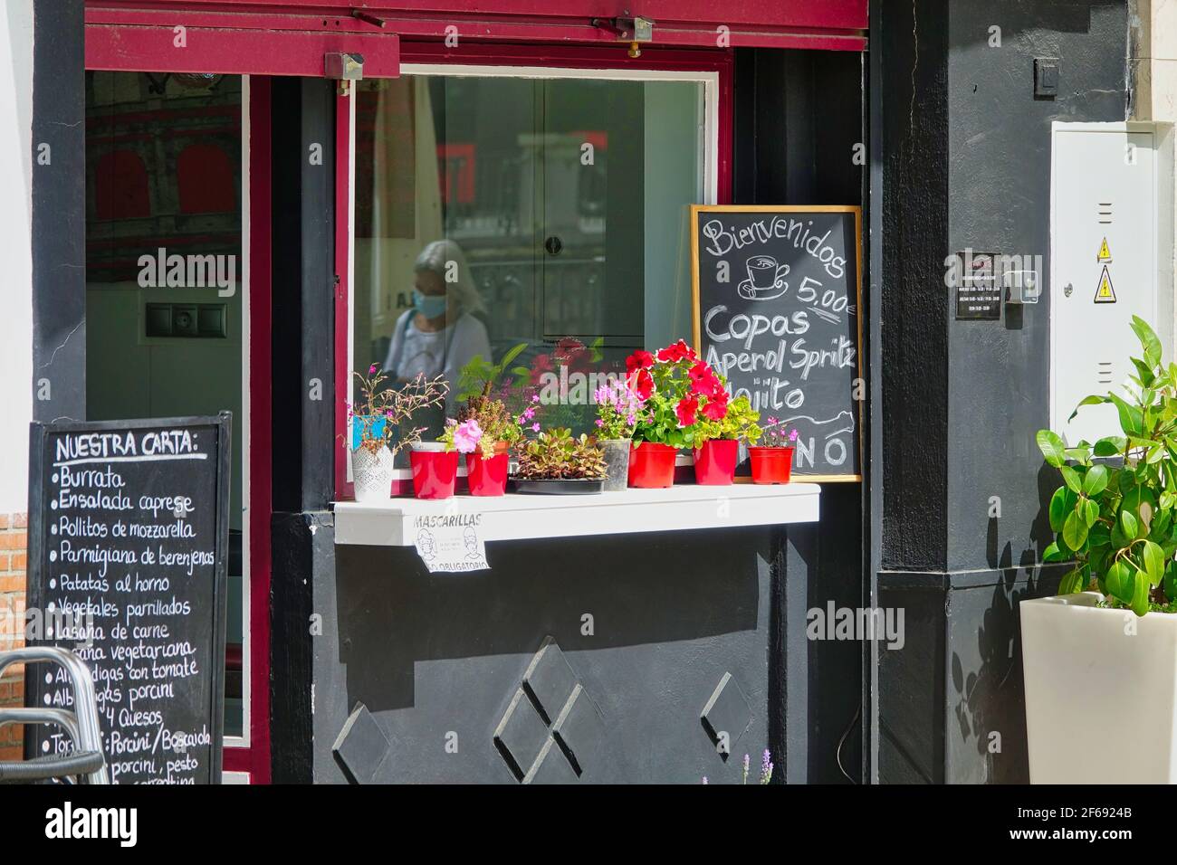 Eingang eines italienischen Restaurants in Granada (Spanien), der für die Öffentlichkeit zugänglich ist, mit dem Spiegelbild einer Frau mit einer Maske im Fenster Stockfoto