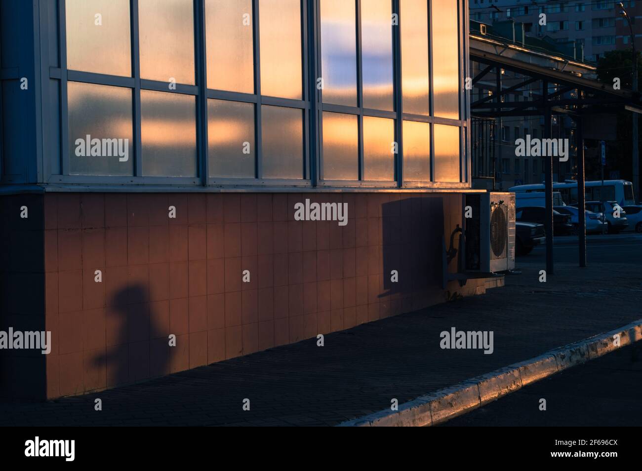Spiegelung des Sonnenuntergangs in den Stadtfenstern, Menschenschatten, dunkelrot-blaue Töne Stockfoto
