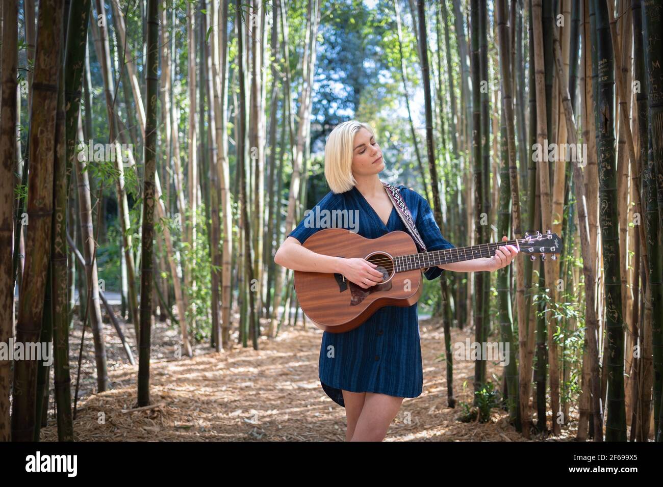 Junge Frau Gitarre spielen und singen in Bambus Waldgarten Stockfoto