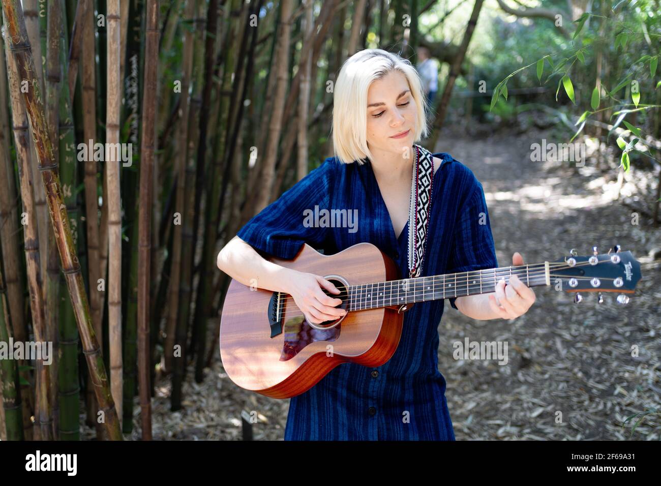 Junge Frau Gitarre spielen und singen in Bambus Waldgarten Stockfoto