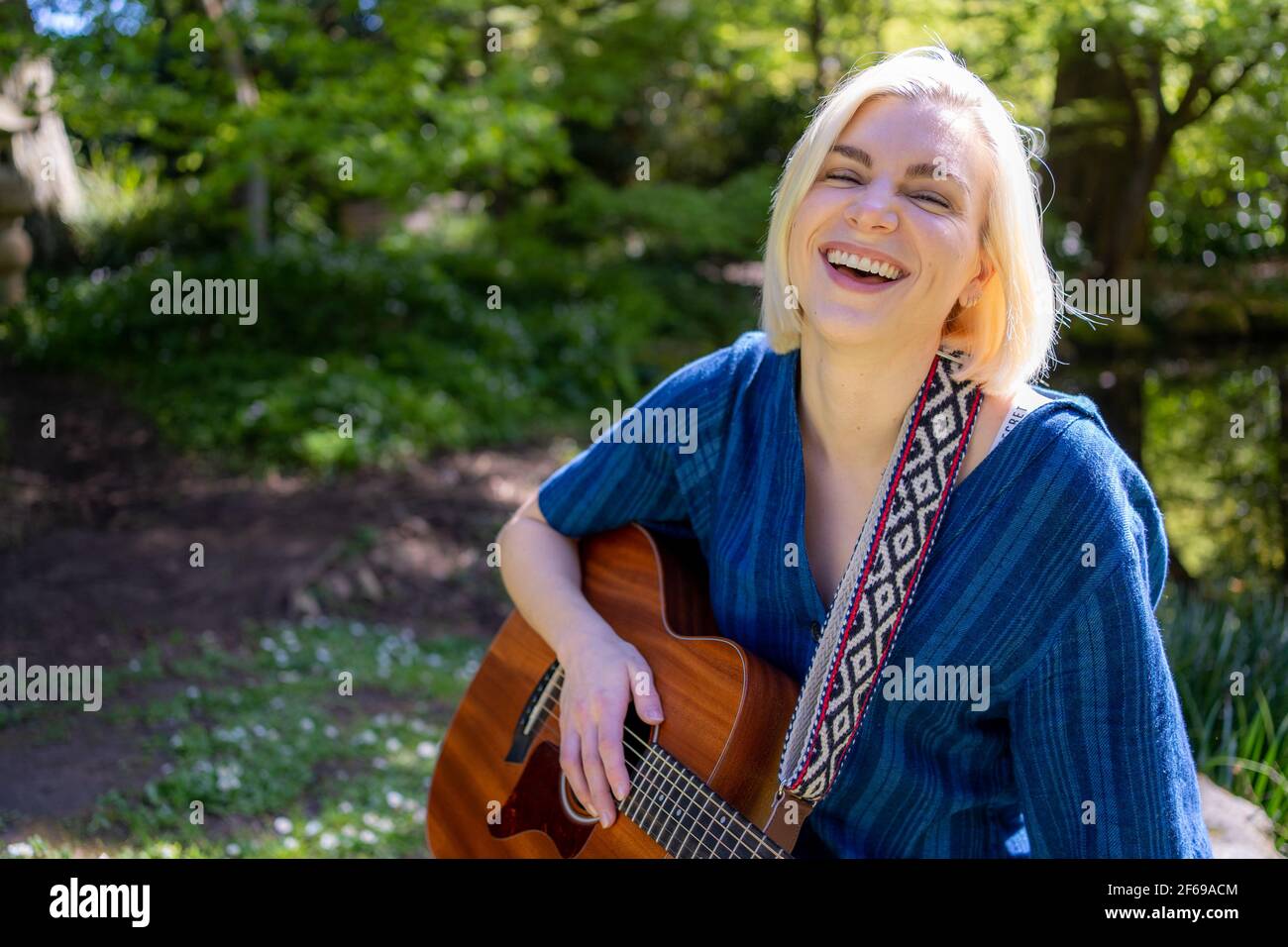 Lächelnde junge Frau spielt Gitarre im japanischen Garten Stockfoto