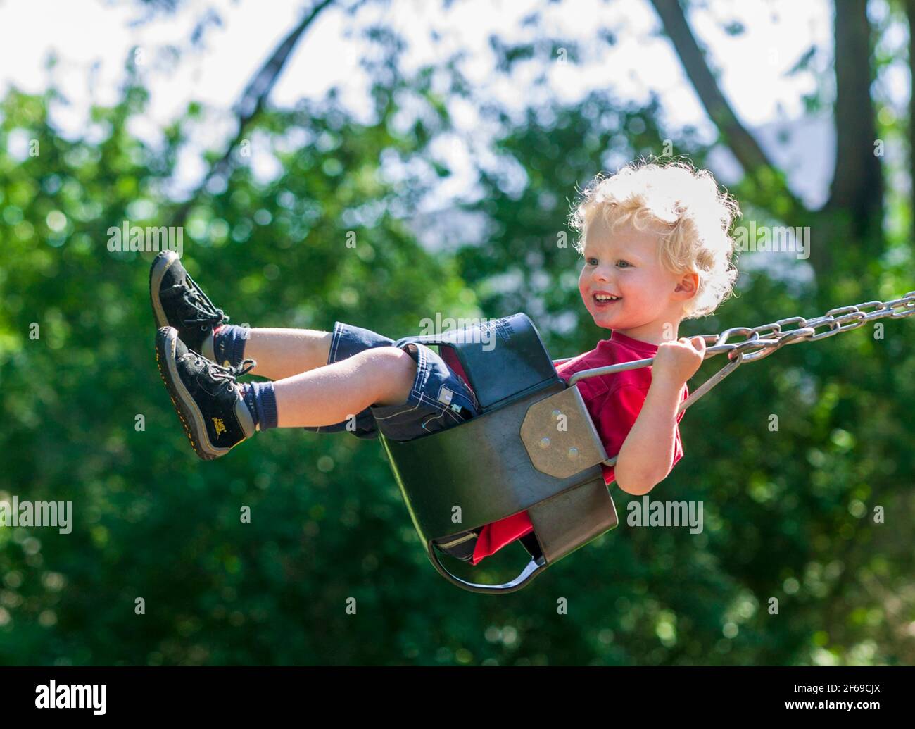 Blonde behaarte Junge spielt auf einer Schaukel in einem Park auf dem Spielplatz. Stockfoto