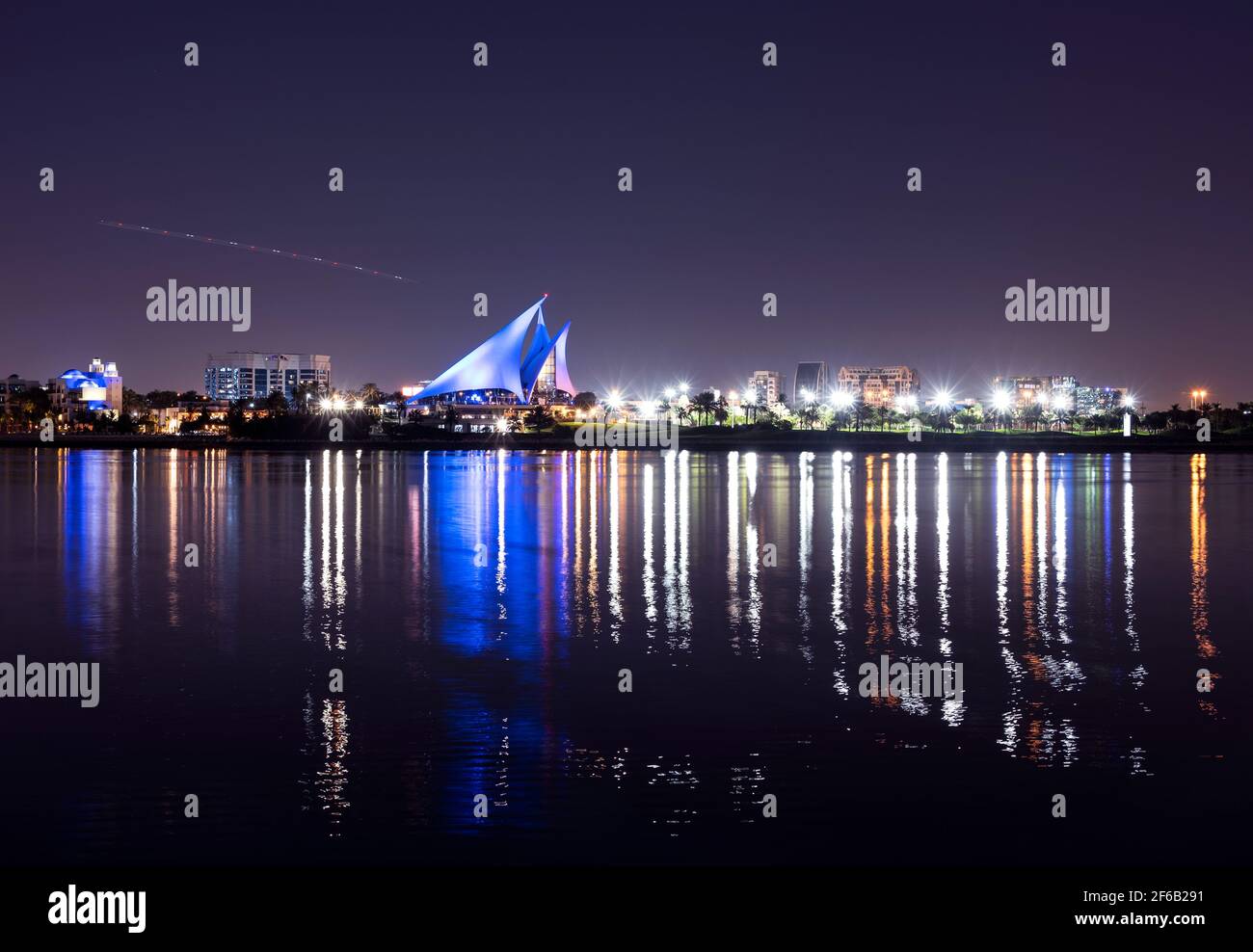 Panoramablick auf das markant segelförmige beleuchtete Clubhaus von Dubai Creek Golf und Yacht Club auf der anderen Seite des Dubai Creek parken Stockfoto