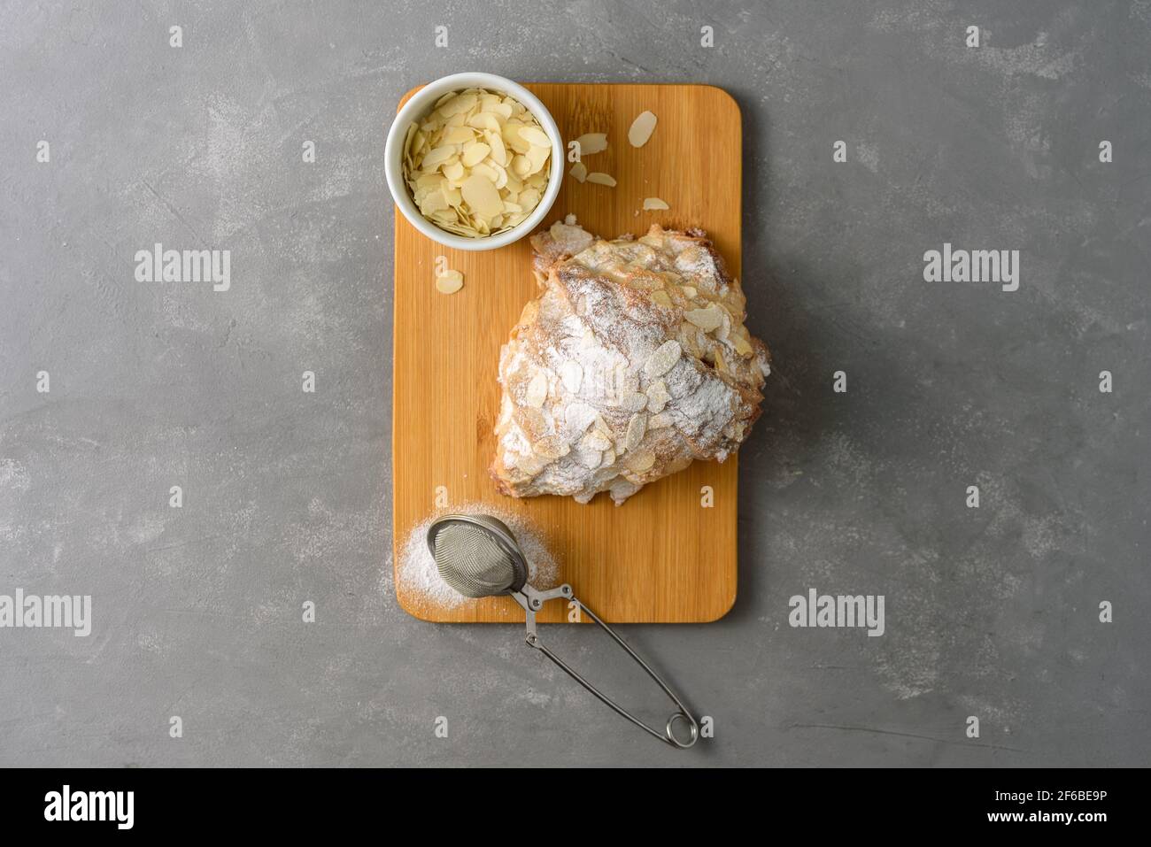 Mandelcroissant auf Holzbrett mit Puderzucker und Mandel Blütenblätter Stockfoto