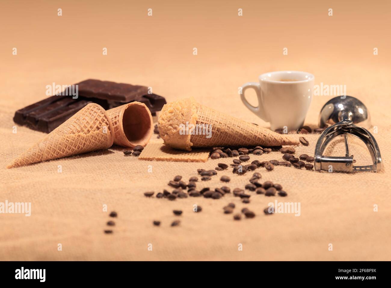 Appetitliches Mandeleis, umgeben von unscharfen Kaffeebohnen, Kaffeetassen und Schokoladenstückchen: Selektiver Fokus. Eiscreme-Konzept. Stockfoto