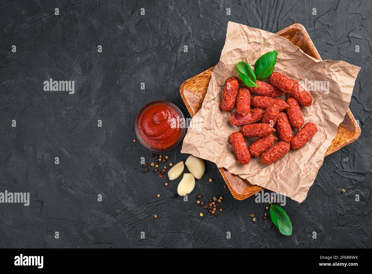 Knoblauch-Mani-Würste mit Sauce auf einem Holzteller auf schwarzem Hintergrund. Stockfoto