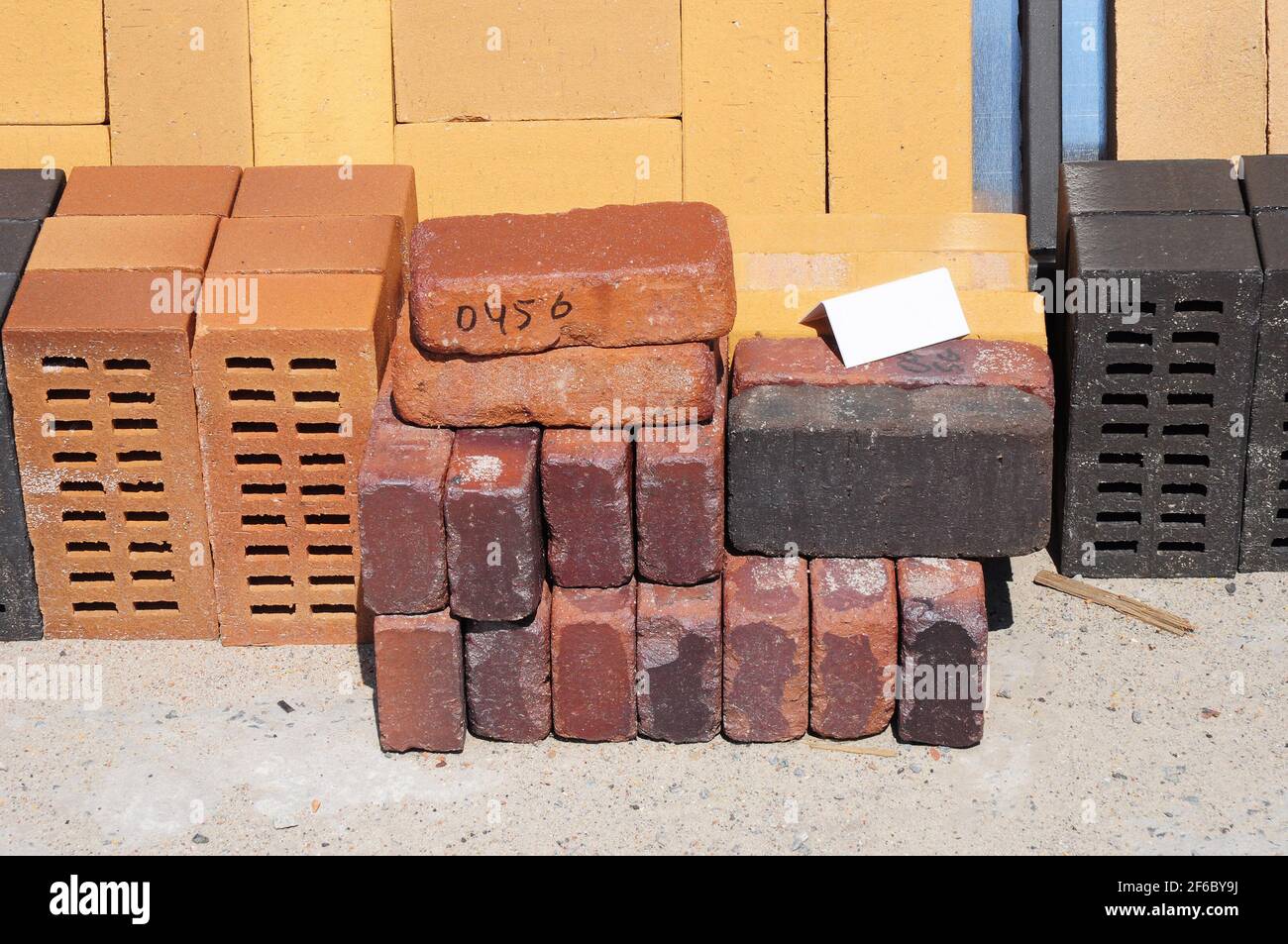 Farbige Bausteine, Ziegelsteine und Betonfertiger (Pflastersteine) oder Terrassenblöcke, die auf Paletten zum Verkauf auf Metallregalen im Freien gelagert werden. Stockfoto