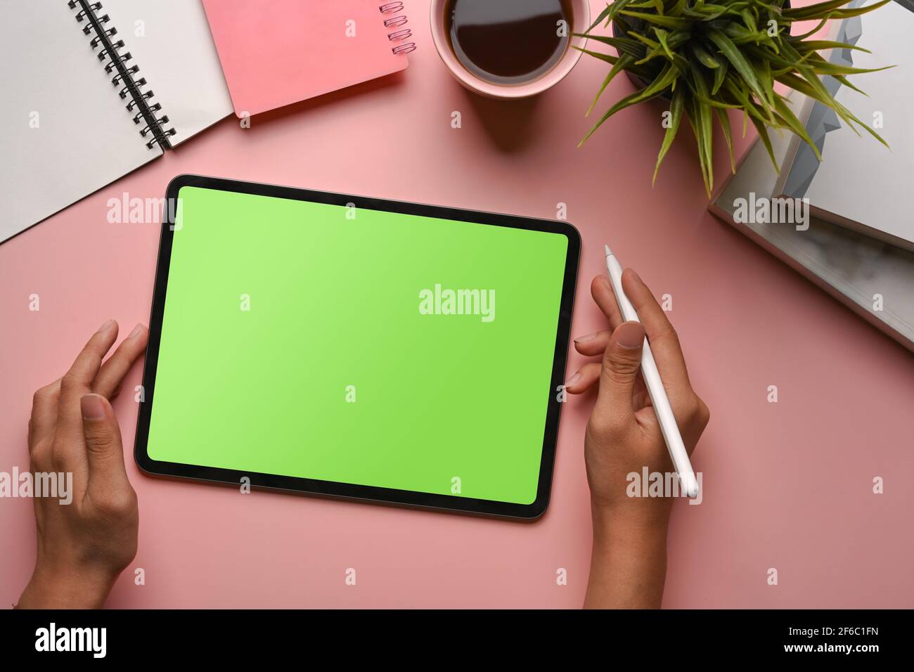Ansicht der weiblichen Hände mit einem digitalen Tablet und einem Eingabestift auf einem rosa, pastellfarbenen Hintergrund. Stockfoto
