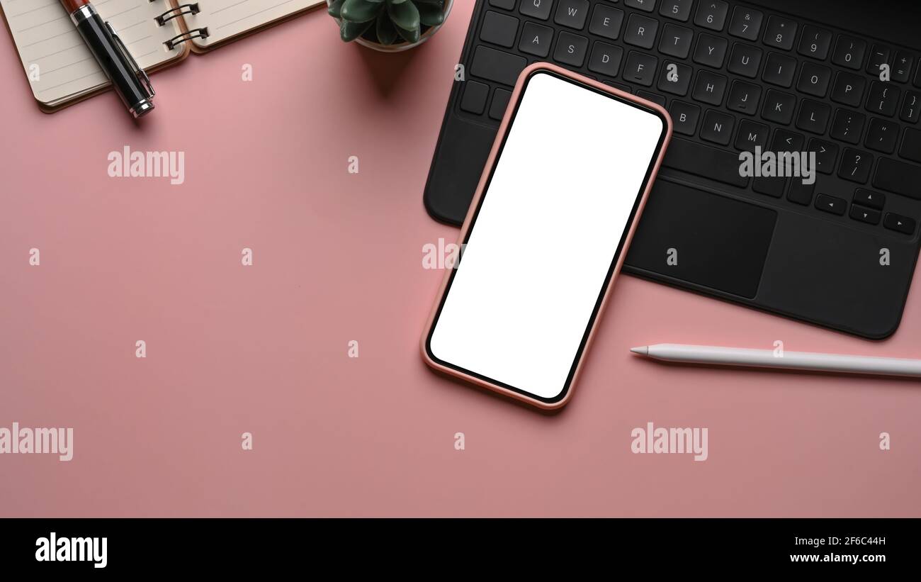 Mobiltelefon mit weißem Bildschirm, Eingabestift, kabellosem Tastenbrett und Notebook auf rosa pastellfarbenem Hintergrund. Femininer Arbeitsplatz. Stockfoto