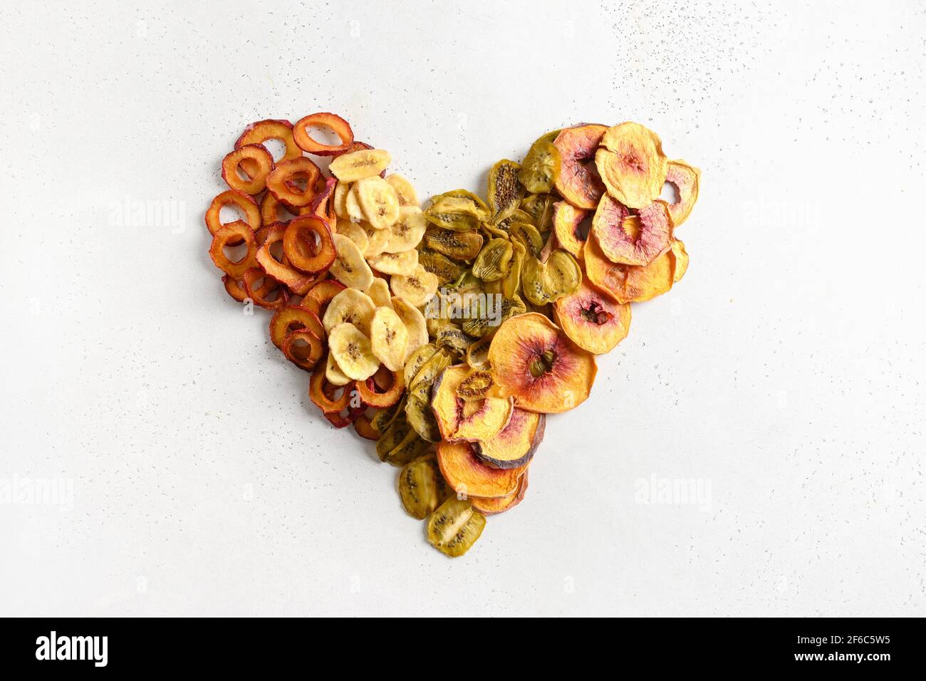 Herz aus getrockneten geschnittenen Pflaumen, Kiwi, Pfirsich-Chips auf weißem Hintergrund. Herbsternte. Heimtrocknung. Snack vegan frei von Zucker Lebensmittel. Stockfoto