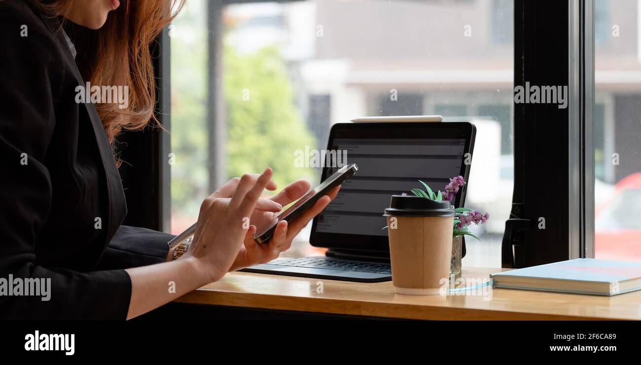 Nahaufnahme der weiblichen Hände mit modernen Smartphone während der Arbeit im Büro mit Computer, Geschäftsfrau Text-Nachricht auf ihrem Handy eingeben. Stockfoto