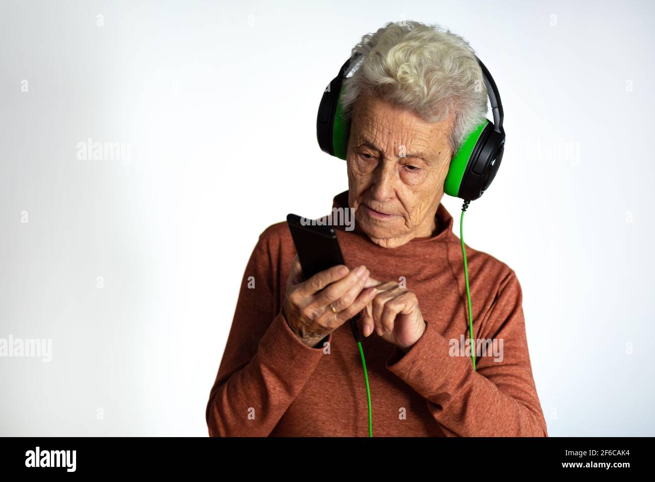 Ältere Frau, die Musik mit Kopfhörern und Smartphone hört. Blick auf Handy-Bildschirm mit Handy-Player-App Online-Musik hören, lernen foreig Stockfoto