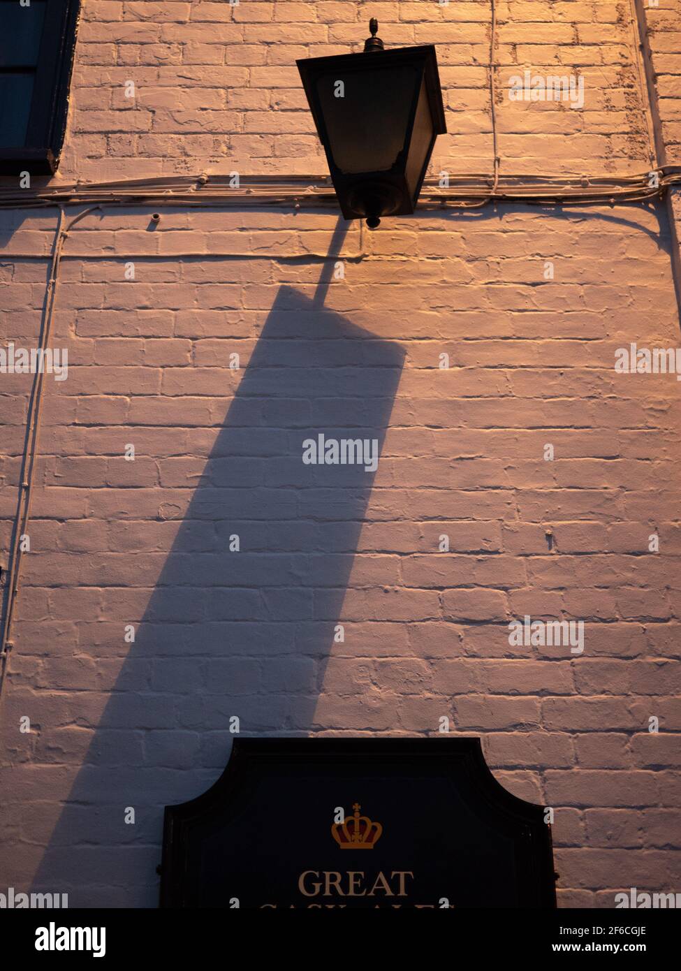 Der Schatten einer unbeleuchteten Laterne, die von einer anderen, moderneren Lichtquelle aus dem Blickfeld in Westbury, Wiltshire, England, Großbritannien, geworfen wurde. Stockfoto