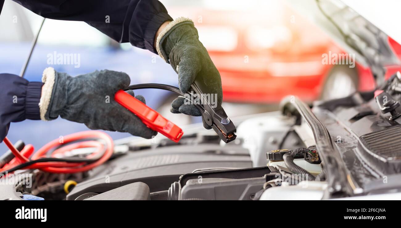 Menschliche Hände mit Überbrückungskabel über dem Automotor in Nahaufnahme. Stockfoto